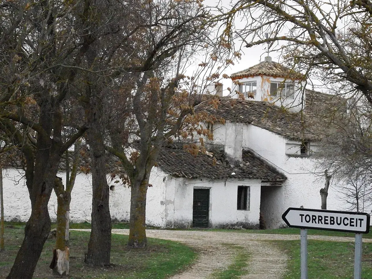 Vista lateral del caserío de Torrebuceit entre árboles, junto a la señal que identifica el lugar